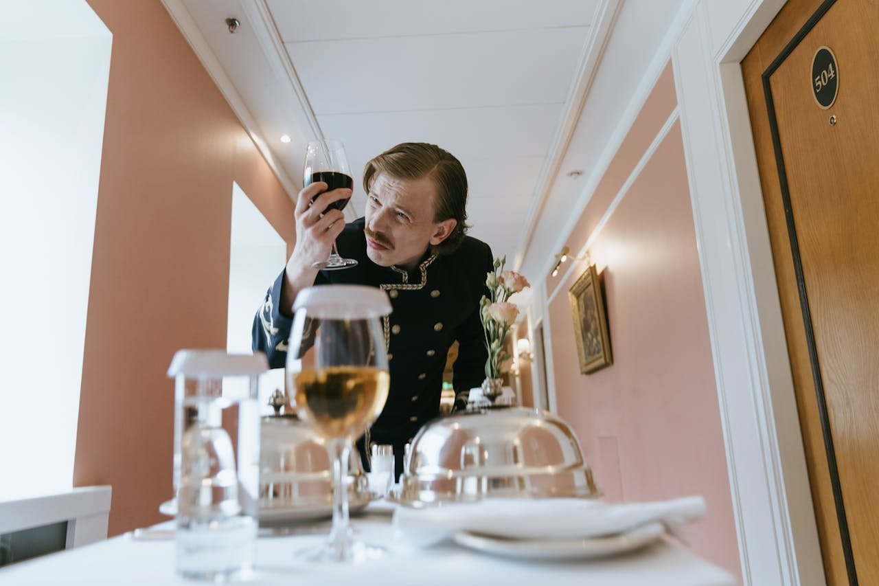 Concierge in uniform examining a drink on a hotel trolley in a corridor.